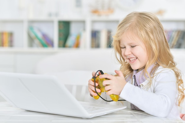 Adorável menina usando laptop em casa jogando jogo