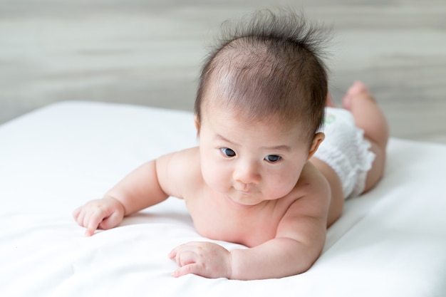 Adorável menino asiático relaxante na cama branca, estágios de desenvolvimento do bebê de 3 meses de idade