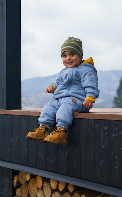 Foto adorável menino em roupas quentes, sentado no terraço ao ar livre