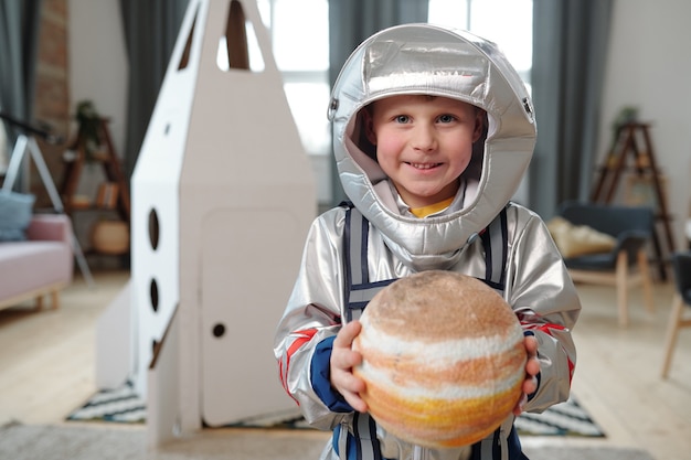 Adorável menino em traje espacial segurando o planeta do sistema solar