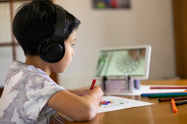 Adorável menino pintando uma mandala com seus marcadores coloridos assistindo a um tutorial em seu tablet