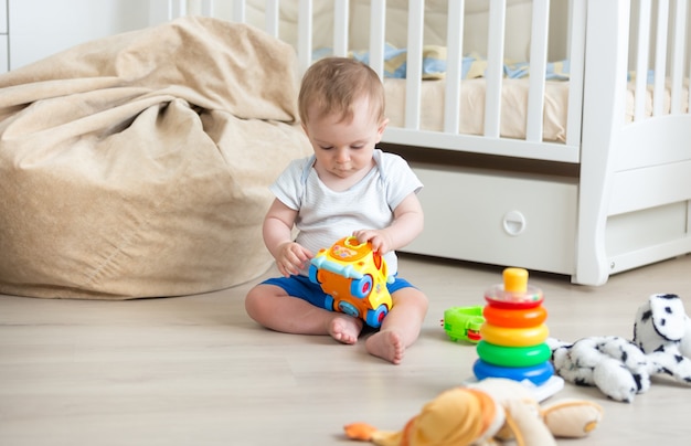 Adorável menino sentado no chão com um carrinho de brinquedo colorido