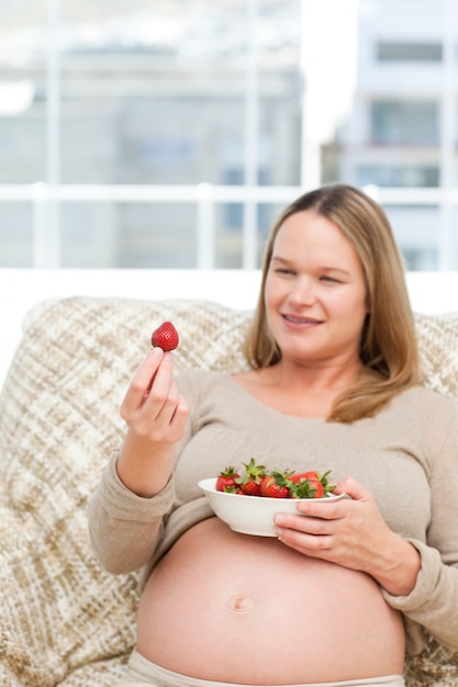 Adorável mulher grávida olhando um morango enquanto relaxa