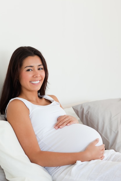 Adorável mulher grávida tocando sua barriga enquanto deita em uma cama