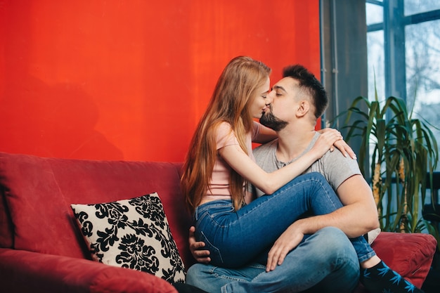 Adorável mulher ruiva beijando o marido, deitado em um sofá e se abraçando