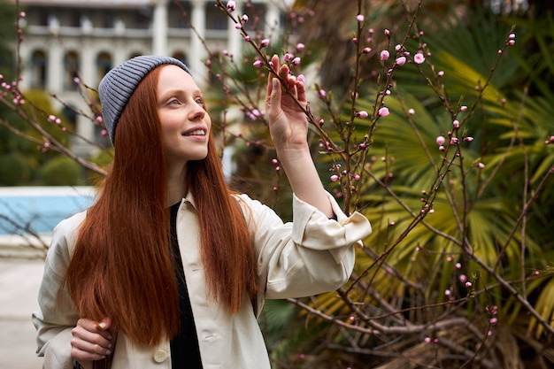 Adorável mulher ruiva com chapéu posando em árvore florescendo na primavera linda jovem feliz enjoyi ...