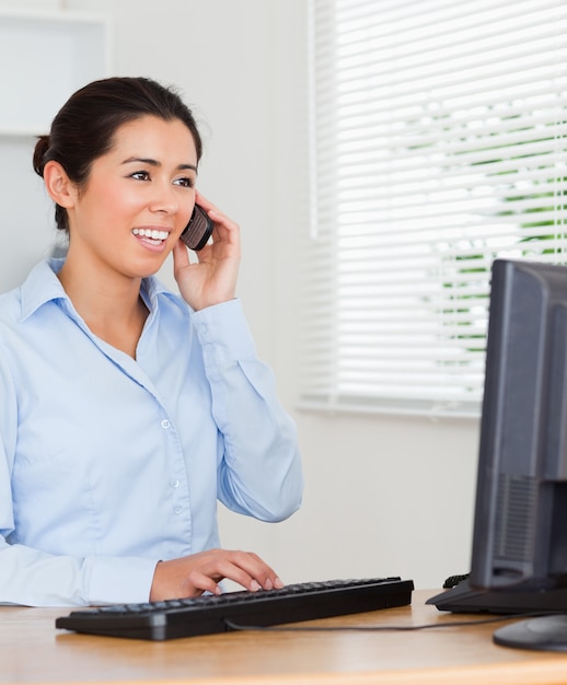 Adorável mulher usando seu telefone celular ao digitar um teclado