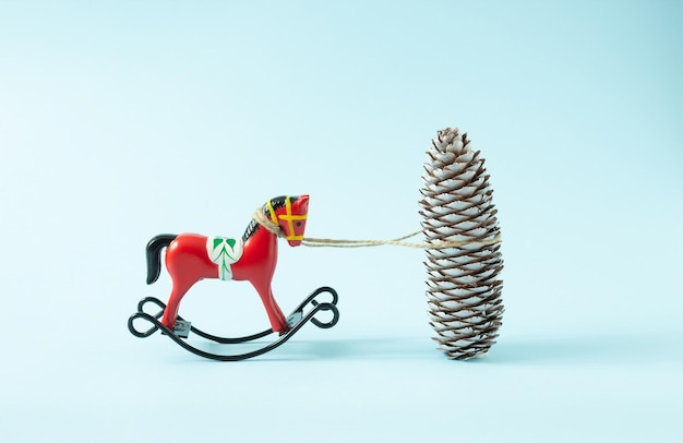 Adorno de caballo balancín de Navidad retro atado a un cono de pino blanco sobre un fondo azul claro Concepto mínimo