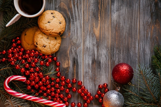 Adorno de Natal e decoração de feriado festivo. bolas brilhantes vermelhas do abeto ramo de árvore doces cana e cordão de grânulo no fundo de madeira. vista superior no café e no biscoito de chocolate.