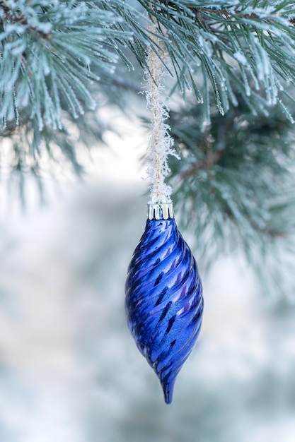 Un adorno navideño azul colgando de un árbol con nieve en las ramas.