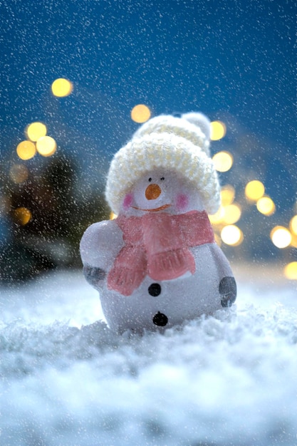 Adorno navideño muñeco de nieve en la nieve y luces bokeh Fondo de temporada de invierno abstracto