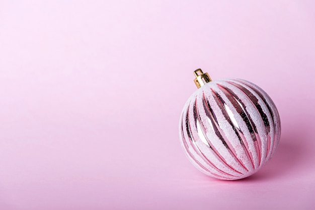 Adorno navideño rosa, bola brillante sobre fondo pastel.