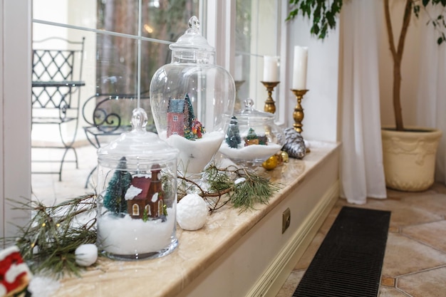 Adornos navideños y de Año Nuevo en el alféizar de la ventana de un loft panorámico Casas de velas en una botella Árbol de Navidad y ramas de pino