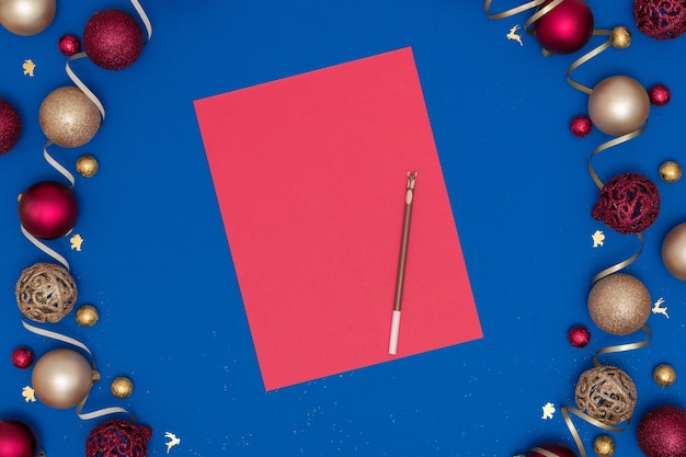 Adornos navideños y de año nuevo y hoja de papel roja en blanco y bolígrafo