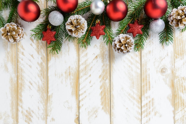 Adornos navideños, bolas rojas y piñas en una mesa de madera blanca. Vista superior, copia espacio.