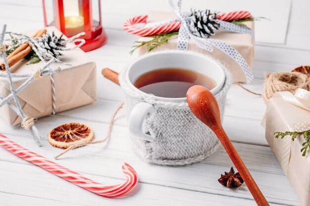 Adornos navideños con cajas de regalo, piñas y una taza de té en madera blanca