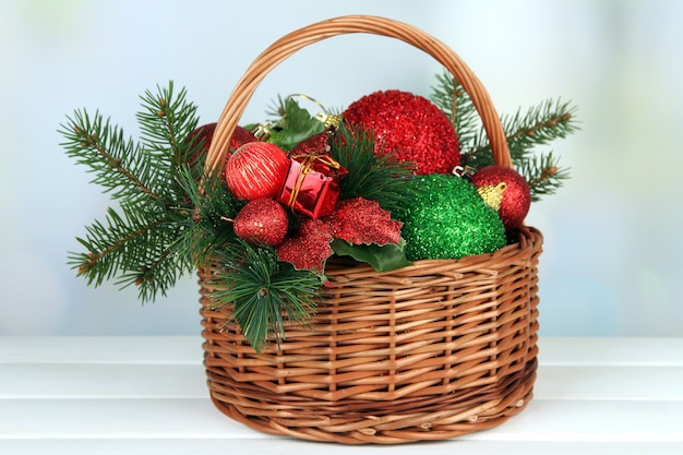 Adornos navideños en canasta y ramas de abeto en mesa sobre fondo brillante