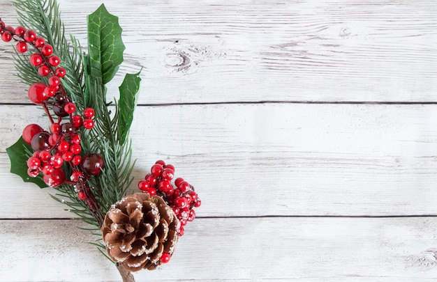 Adornos navideños hechos de ramas de abeto con frutos rojos y conos de pino natural marrón sobre un fondo de madera clara.