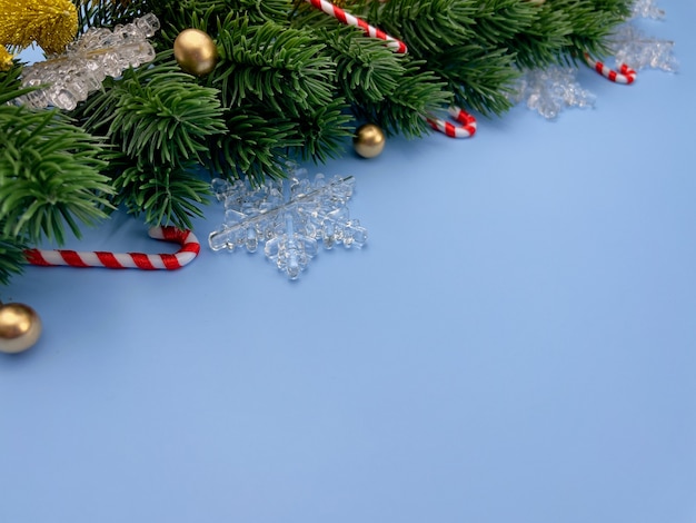 Adornos navideños hojas de pino copos de nieve bolas doradas sobre fondo azul.