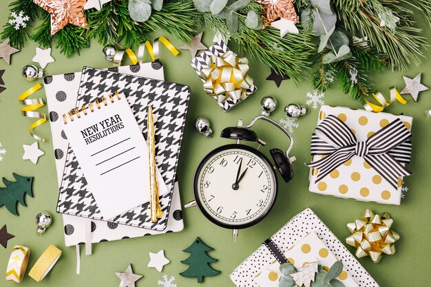 Adornos navideños de invierno, cuadernos con reloj despertador y regalos sobre fondo verde. Endecha plana, vista superior