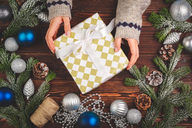 Adornos navideños en mesa de madera con regalo decorado en manos de mujer