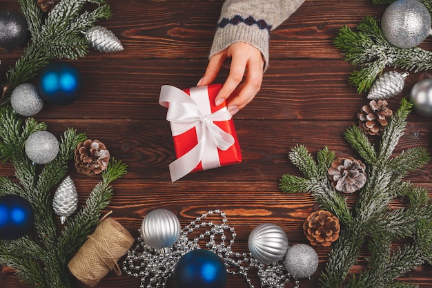 Adornos navideños en mesa de madera con regalo decorado en manos de mujer