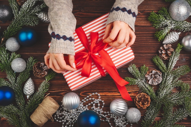 Adornos navideños en mesa de madera con regalo decorado en manos de mujer