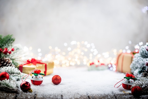 Adornos navideños rojos sobre la nieve con cajas de regalo, ramas de abeto y luces navideñas