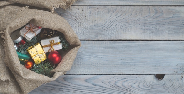 Adornos navideños en un saco sobre una superficie de madera blanca. Vista superior