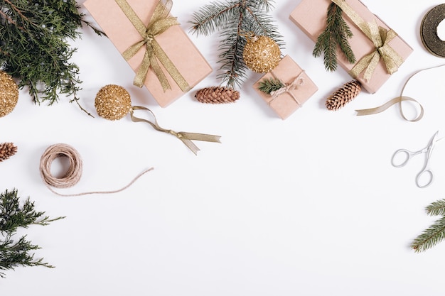 Adornos navideños sobre fondo blanco: ramas de abeto, cajas de regalo, cintas, juguetes, cuerdas, tijeras.