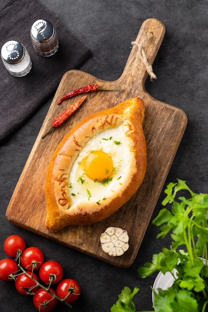 Adscharisches Khachapuri-Gericht Traditionelles georgisches Essen aus hausgemachtem Brot mit Käse und Eigelb auf einem Holzbrett mit Tomaten und frischer Kräuterdraufsicht