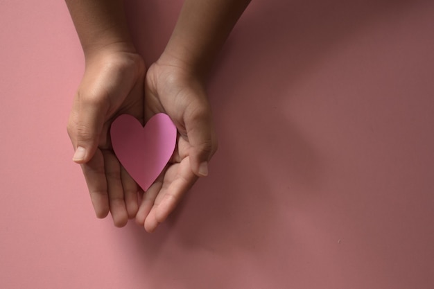 Adulto e criança com mãos segurando um coração rosa sobre fundo rosa amor saúde seguro familiar