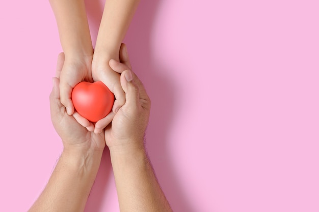 Adulto e criança mãos segurando coração vermelho isolada em rosa