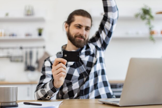 Adulto emocional com cartão de débito levantando o punho enquanto olha felizmente para o computador