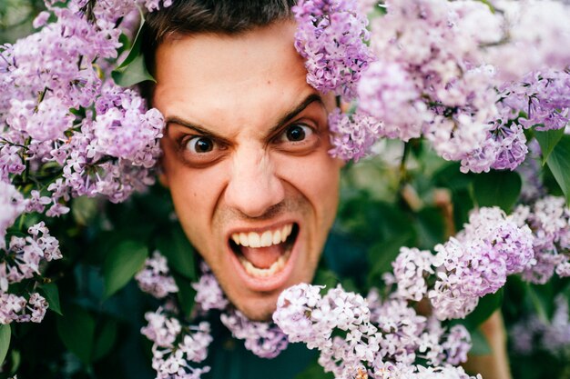 Adulto hombre divertido rostro mueca rodeado de flores florecientes.
