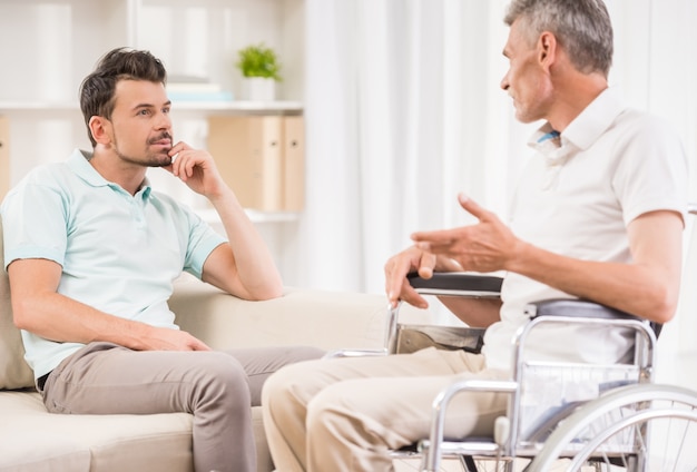 Adulto homem sentado em casa e conversando com seu pai mais velho.