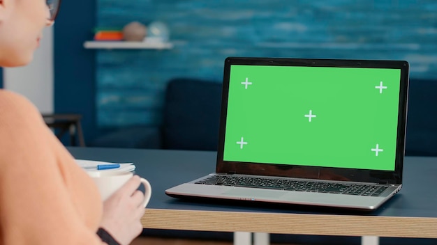 Adulto joven analizando la pantalla del portátil con pantalla verde en la sala de estar, usando una plantilla de maqueta con espacio de copia aislado y fondo de clave chrma en blanco en la computadora. Estudiante de escuela remota