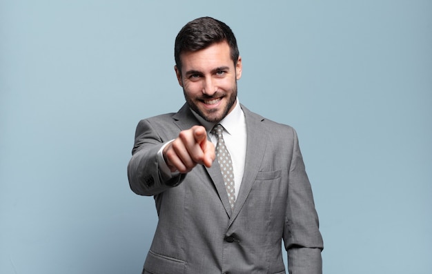 Adulto joven apuesto hombre de negocios apuntando al frente con una sonrisa satisfecha, confiada y amistosa, eligiéndote