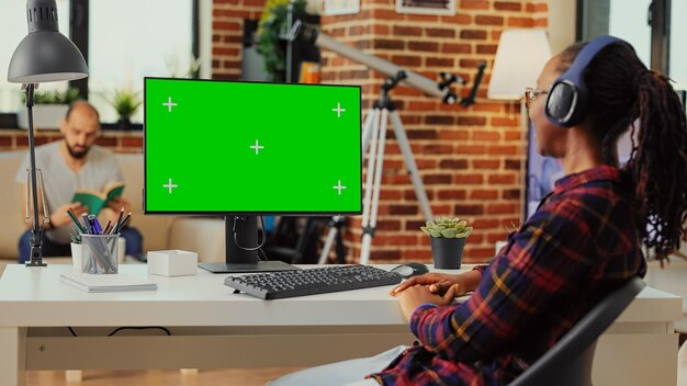 Foto adulto joven con auriculares mirando la pantalla verde, escuchando música con auriculares y trabajando con una plantilla de maqueta aislada. usando el espacio de copia de la clave de croma en el monitor de la computadora.