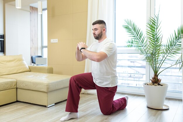 adulto joven barbudo haciendo ejercicios de estiramiento en casa en la sala de estar viendo una lección en video o un tutorial en línea usando una computadora portátil Hombre haciendo fitness y deportes por la mañana sentado en el piso