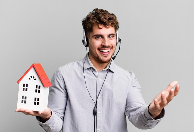 Adulto joven caucásico agente inmobiliario con auriculares y un modelo de casa