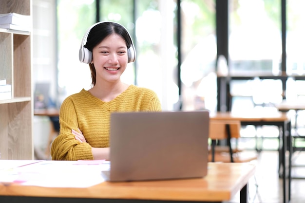 Adulto joven feliz sonriente estudiante hispana asiática usando auriculares hablando en una reunión de chat en línea usando una computadora portátil en el campus universitario o en la oficina virtual Estudiante universitaria aprendiendo de forma remota