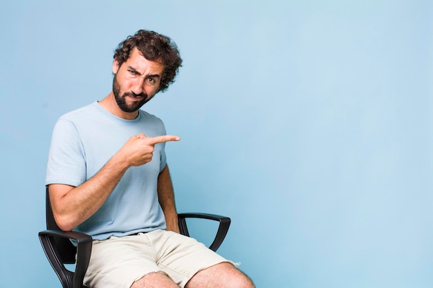 Adulto joven hispano loco sentado en un concepto de espacio de copia de silla