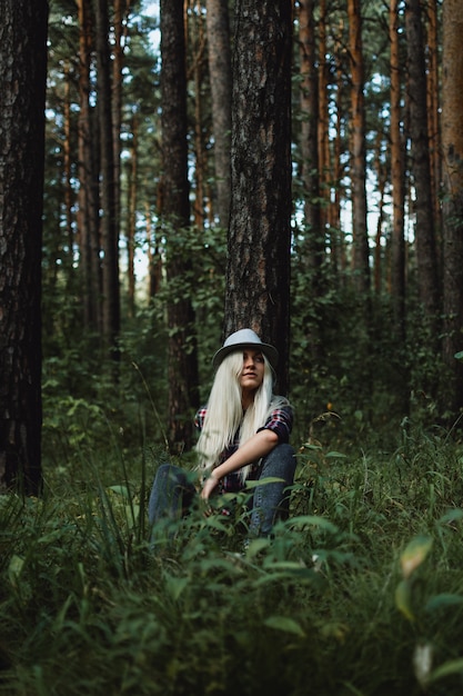 Adulto joven mujer rubia con un sombrero sentado en el bosque