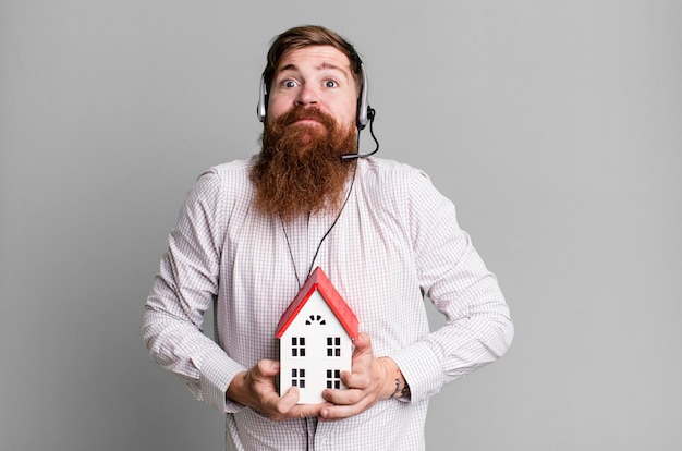 Foto adulto joven pelirrojo barbudo genial agente inmobiliario hombre con un modelo de casa