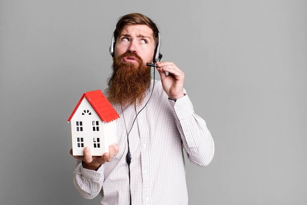 Foto adulto joven pelirrojo barbudo genial agente inmobiliario hombre con un modelo de casa