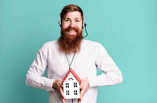 Adulto joven pelirrojo barbudo genial agente inmobiliario hombre con un modelo de casa