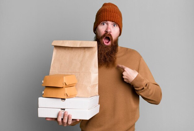 Adulto joven pelirrojo barbudo hombre fresco con una bolsa de papel con comida para llevar