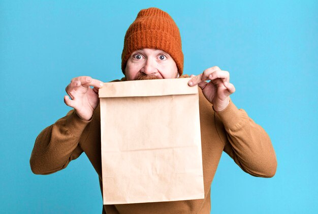 Adulto joven pelirrojo barbudo hombre fresco con una bolsa de papel con comida para llevar