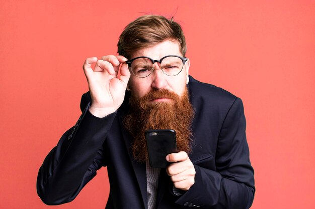 Adulto joven pelirrojo barbudo hombre de negocios fresco usando su teléfono inteligente